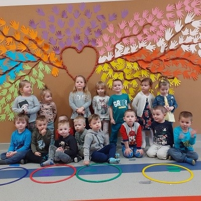 zdjęcie grupowe na tle kolorowego drzewa z wyciętych przez dzieci papierowych dłoni 