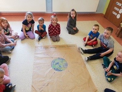 Dzieci siedzą przed plakatem z okazji dnia ziemii