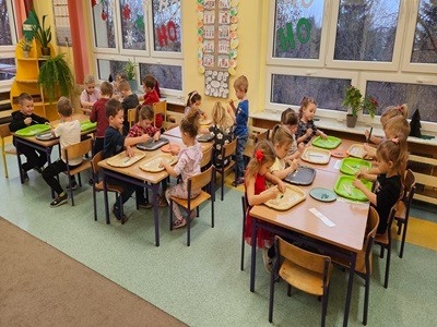 Dzieci z grupy przedszkolnej tworzą ozdoby choinowe i wieszają je na przedszkolnej choince