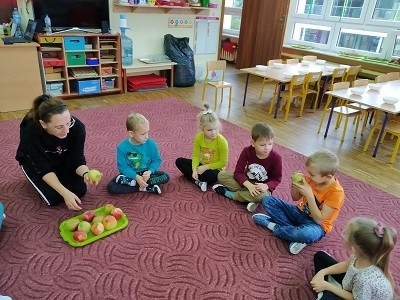 dzieci siedzą w kole wokoło jabłke 